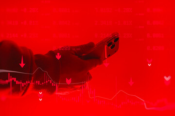 Hand holding smartphone with trading data and falling market charts on red background. Concept of financial crisis, stock market crash, crypto trading loss and investment risk.