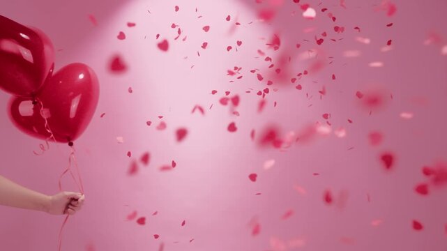 A Hand Grasping Heart - shaped Balloons and Confetti