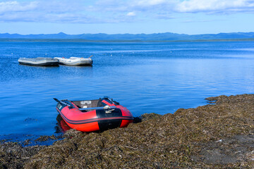 Bright red inflatable boat rests on the shore of a calm, blue water bay surrounded by mountains