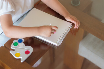 Niña pintando con acuarelas sobre una mesa de vidrio