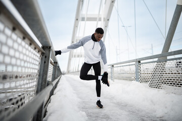 African american man stretching on snowy bridge