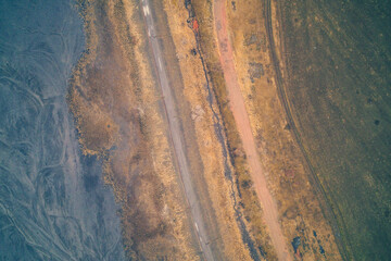 Parallel asphalt road and red dirt track near toxic waste, industrial boundary concept, aerial drone shot top view