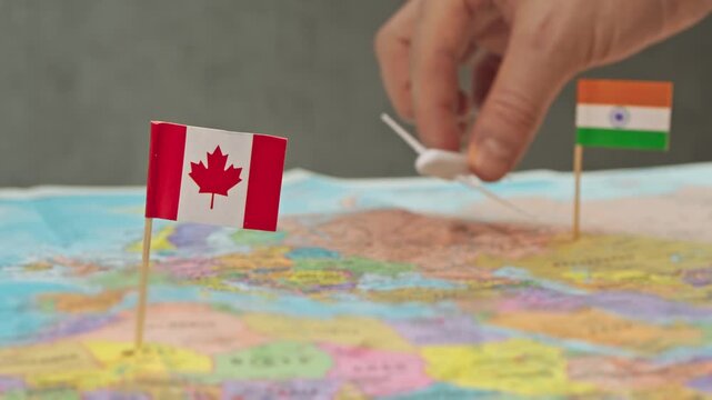 Toy airplane between India and Canada flags above political world map, symbol diaspora travel, student traffic, code share flights and growing connectivity of Canada with India.
