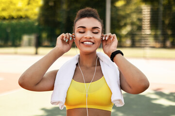 Workout Playlist. Portrait of satisfied fit African American woman wearing putting on earphones...