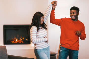 Naklejka premium A couple enjoys a fun moment, dancing together in a warm indoor setting with a fireplace. They are smiling and holding hands, clearly enjoying their time together.