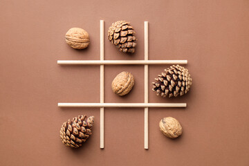 Tic tac toe game made with walnuts and cones on beige background, flat lay