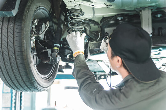 A male car mechanic performing maintenance, inspection and work under a vehicle going up on a lift