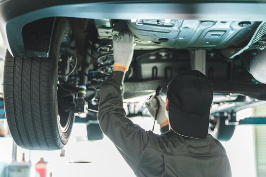A male car mechanic performing maintenance, inspection and work under a vehicle going up on a lift