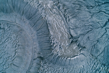 Abstract blue gray mudflow texture with deep cracks and frozen landslide patterns, cold industrial wasteland background aerial top down view