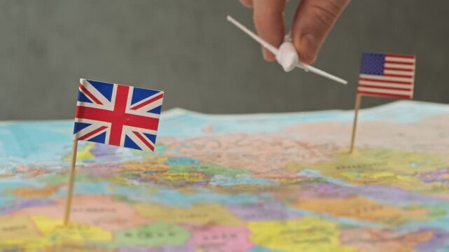 Toy airplane flying from United Kingdom to United States above world map, symbol long haul flights, tourism, study abroad and business travel across Atlantic Ocean.