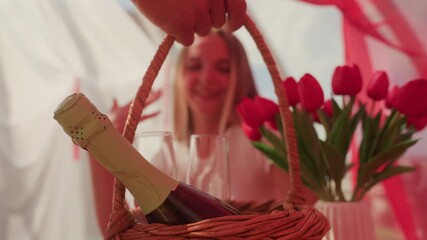 blonde caucasian woman joyful bridal celebration with net veil and tulip bouquet, wicker basket holding champagne bottle and flutes, hands placing veil while she laughs and reaches for glass, intimate