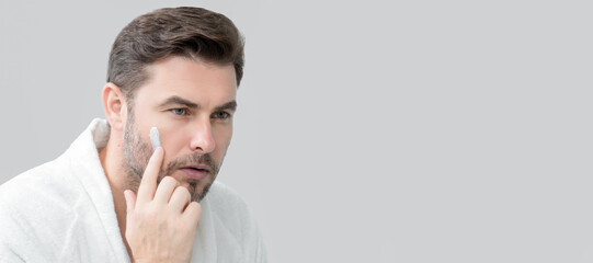 Fototapeta premium Banner of beauty male portrait of a beautiful man applying face cream. Moisturizing skincare cream for man. Mask for skin lifting and anti-aging effect. Beauty male face concept. Skincare and aging.