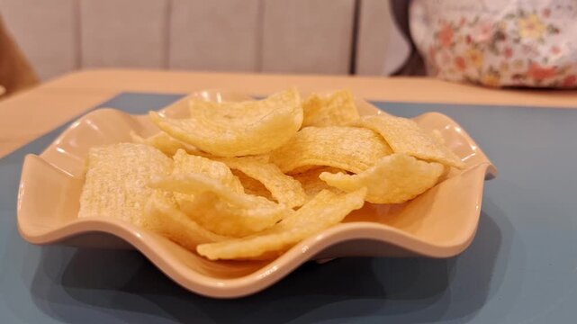 Crackers or Kerupuk inside a wavy-edge bowl in a similar color on the table waiting to be nibbled