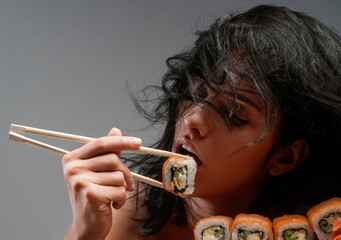 Sexy woman eating sushi with chopsticks. Sensual woman tasting sushi. Sexy girl enjoying seafood...