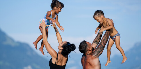 Happy family on summer. Parents toss children up in air. Loving family. Parents lift children up. Summer with kids. Caring family. Parents throw kids up and catch them on sky. Excited family outdoor.