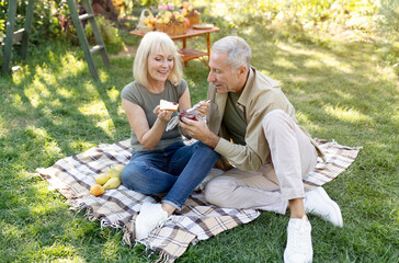 Cute retired couple having picnic in their garden, sitting on blanket and eating toasts with jam, spending time together outdoors and enjoying warm spring day