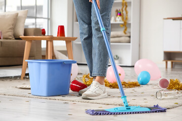 Young woman mopping floor in messy room after party