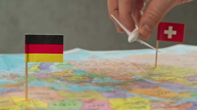 Toy airplane flying from Germany to Switzerland above colorful world map, symbol ski holidays, business trips, scenic flights and frequent regional air travel.