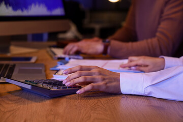 Female business analyst's hands working with calculator in office at night, closeup. Data science concept