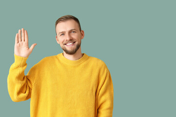 Young man in yellow sweater waving hand on green background