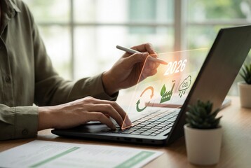 Corporate professional using laptop with 2026 sustainability hologram for green energy planning