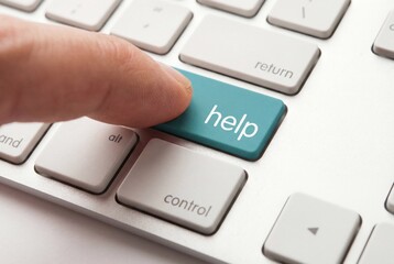 Human finger pressing a teal help key on a computer keyboard for online technical support