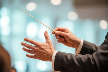 Closeup of male hands holding a baton and directing a musical performance in a concert hall