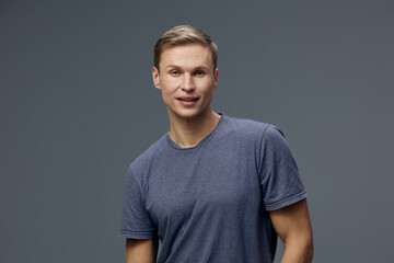 Smiling young man with short light brown hair in casual blue t-shirt looking at camera isolated on...