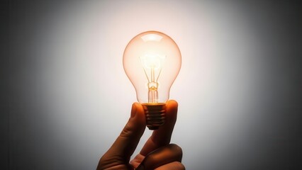 A hand dramatically holds a glowing orange light bulb, captured in a close-up shot against a gradient gray background, symbolizing a bright new idea.