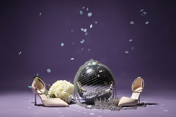 Stylish high heels with disco ball, tiara and flowers on lilac background