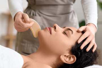 Fototapeta premium Young African-American woman getting facial massage with guasha in spa salon, closeup