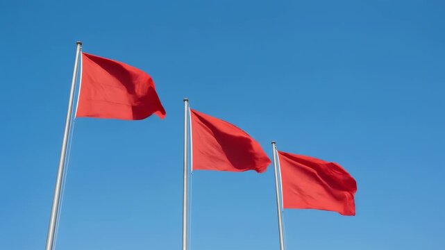 Three vibrant red flags waving against a clear blue sky, symbolizing alertness and warning in outdoor settings.