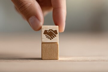 Human finger placing a wooden block with a handshake icon symbolizing partnership and agreement.