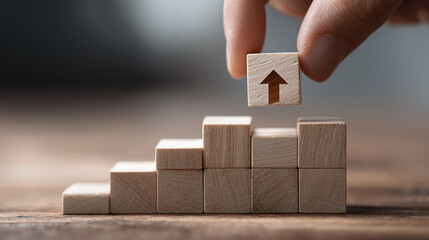 A hand placing the final block with an upward arrow on top of a staircase made of wooden blocks, symbolizing growth and progress