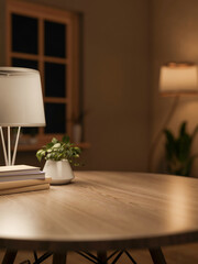 Books and desk lamp aside potted planted on round wooden table across window in modern living room.