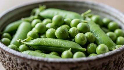 Vibrant green snap peas and shelled peas covered in water droplets in a textured ceramic bowl.