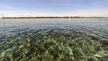 Crystal-clear turquoise waters with coral reef visible beneath the surface, with the coastline of Semporna, Sabah in the background.