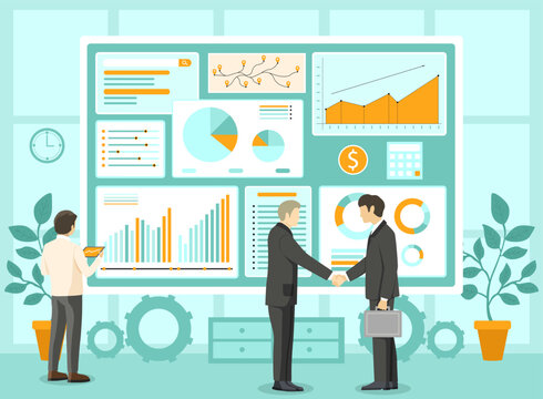 Two people shaking hands in office setting. One person standing near large screen showing graphs and charts