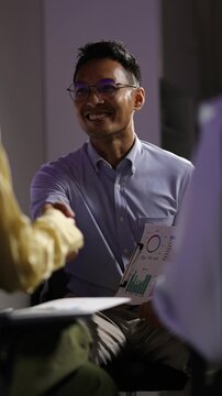 Asian employee explaining company statistics during a late-night business meeting. A diverse team is collaborating on the project.