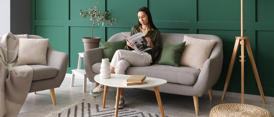 Obraz premium Beautiful woman reading magazine on grey sofa in living room