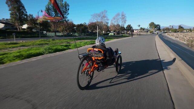 Elderly man rides an electric trike along a smooth road near homes on a bright day.