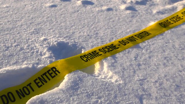 Low angle closeup of yellow crime scene tape fallen on snow covered landscape with boot prints and gentle wind, abandoned winter investigation scene. Cold trace on snowy terrain with shallow depth