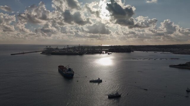 Drone view of the Malta Freeport in Birżebbuġa harbor, featuring industrial port facilities, aquaculture setups, and maritime activity along the Mediterranean coast under a cloudy winter sky.