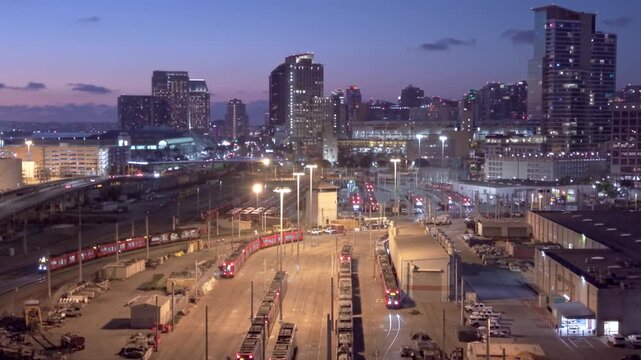 San Diego California skyline at night with high-rise buildings and trolley driving, slow drone pullback shot.