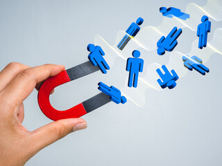 Conceptual image of a hand holding a red magnet attracting 3d blue human icons, symbolizing customer attraction, marketing strategy, lead generation, sales funnel, and business growth.