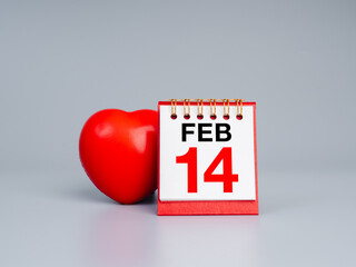 Front view of desk calendar showing February 14 and red heart ball on gray background. Perfect for Valentine's Day themes concept, romantic promotions, and love-related content or advertisements.