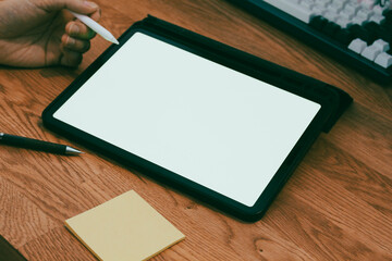 A businessman using digital tablet with blank white screen at wooden desk, productive work from home and remote office mockup concept.