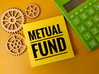 Sticky note with the text "MUTUAL FUND" next to a calculator and some wooden gears