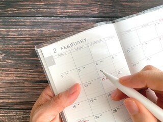 Woman's hand filling out February schedule book on wooden table