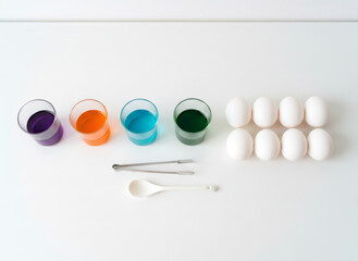 Raw eggs and colorful dye in glasses on white table for Easter egg decoration. Family fun activity for holiday celebration. Spring tradition.